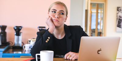 Woman looking frustrated while sitting at her desk with a laptop and a cup of coffee