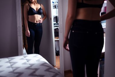woman in black pants and black bra looks at her image in a mirror 