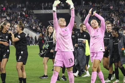 women in a soccer field wearing black and pink uniforms waving to their fans
