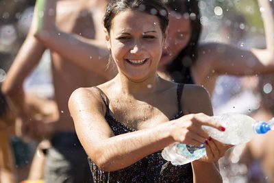 smiling woman throwing water from a bottle, with people behind her out of focus