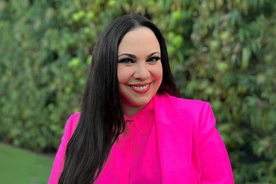 Photo of Gloria Calderón Kellet in a pink blazer and blouse with a green background