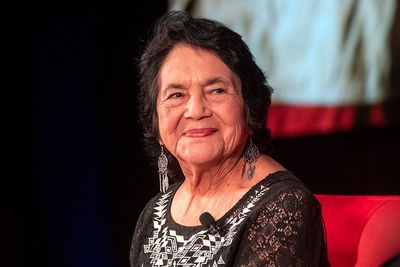 Dolores Huerta smiling sitting on a red couch 