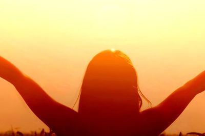 A woman extending her arms to the sky during sunset