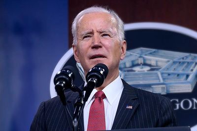President Biden Stands at a Podium Speaking into Mics