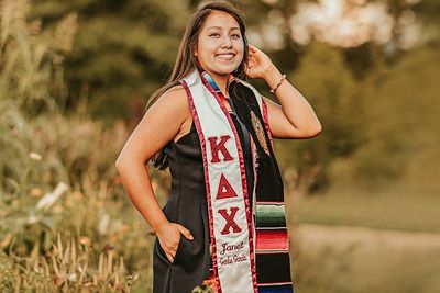 A girl in her greek life academic regalia standing in a field