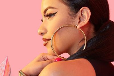 Latina woman wearing large hoop earrings, set against a vibrant, colorful backdrop