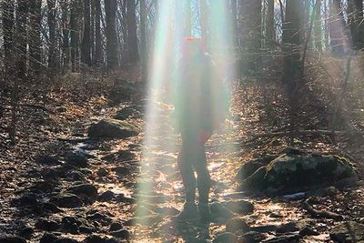 Woman standing under a ray of sunshine in the middle of the forest 