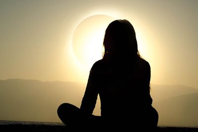 silhouette of a cross-legged woman facing a solar eclipse