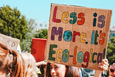 girl holding up a cardboard sign that says: less is more, it's eco-logical