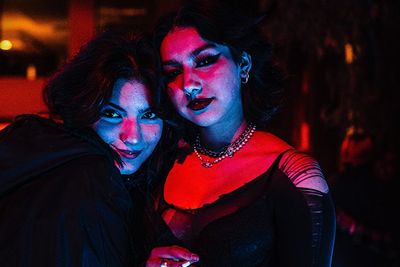 two goth girls in dark clothing and makeup smiling in moody lighting
