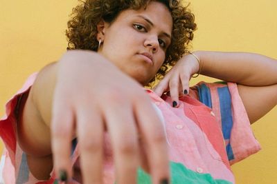 Portrait of a vibrant Latin woman in a colorful shirt against a sunny yellow backdrop.