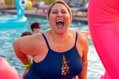 woman in a blue swimsuit sitting on a pink flamingo inflatable in a pool and laughing out loud