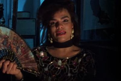 a screengrab from the documentary film Paris is Burning showing Angie Xtravaganza in a dimly lit room holding a fan