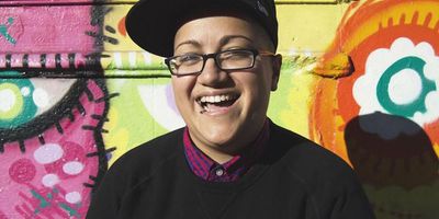 Picture of Gabby Rivera laughing in front of a colorful wall.
