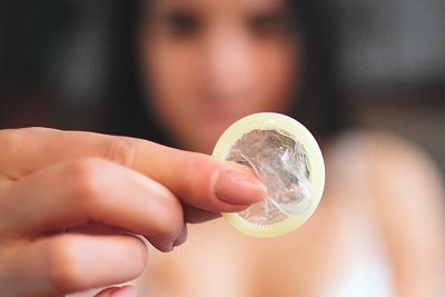 Woman confidently holding a condom between her fingers, promoting safe sex practices