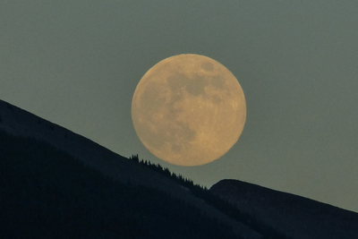 a full moon above the dark silhouette ridge of a mountain 