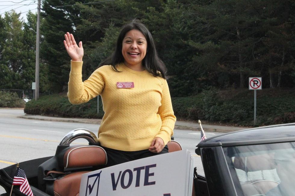 Woman smiling in the back of a convertible with a sign that says "Vote".