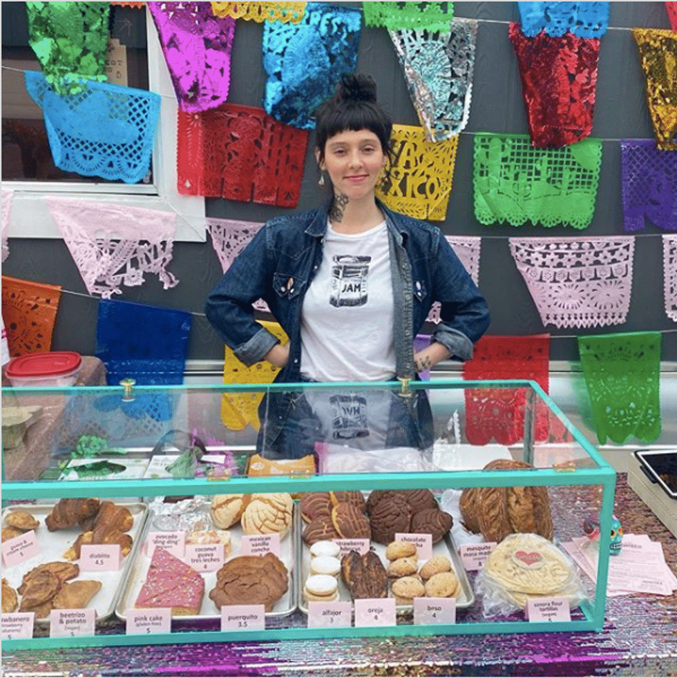 woman, Mariela Camacho, standing in front of a case of pastries